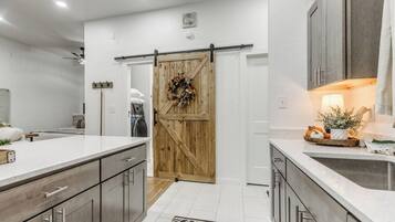 Cozinha moderna com porta de madeira central, bancadas brancas e tapete preto e branco.