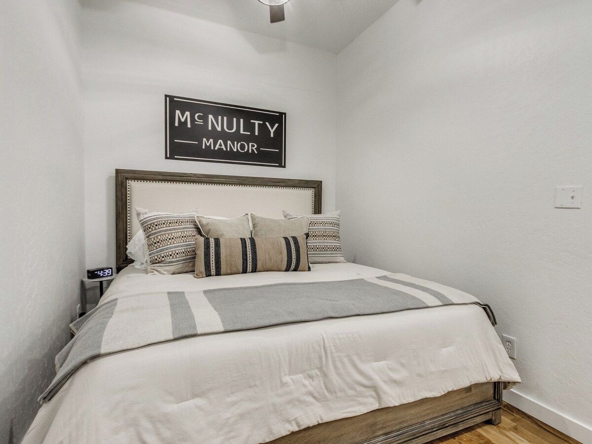 Ein Schlafzimmer mit einem Bett, Kissen, einer Decke, einem Schild über dem Bett und einer Wanduhr.