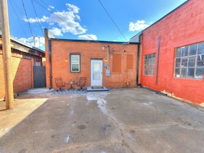 A red brick building with a door, windows, and a small outdoor seating area with chairs and a table.
