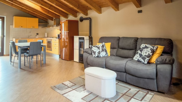 A modern living room with a grey sofa, a dining table with chairs, and a kitchen in the background. - Abri Douillet (Saint-Marcel)