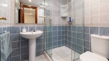 Une salle de bain avec un lavabo sur colonne, une cabine de douche en verre et des toilettes.