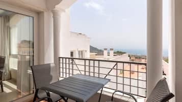 A balcony with a table and chairs, offering a view of the sea and buildings.