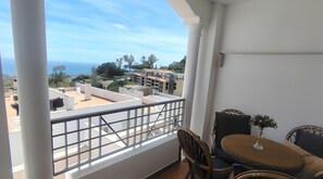 A balcony with a view of buildings and the sea. There is a table with chairs and a vase of flowers. - Apartment 'Luz Penthouse' with Sea View, Private Terrace and Wi-Fi (Mijas)
