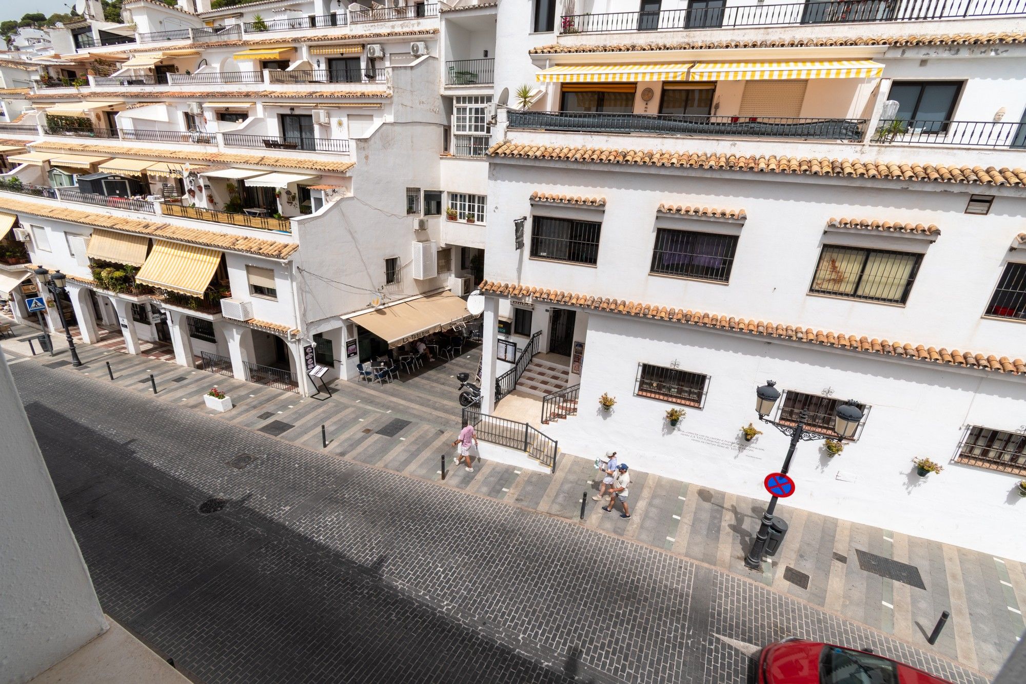 Un edificio de varios pisos con balcones, mobiliario exterior y una calle peatonal.