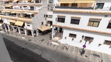 Un edificio de varios pisos con balcones, mobiliario exterior y una calle peatonal.