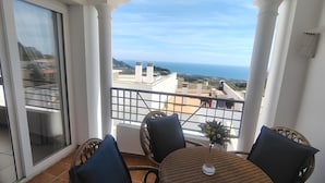 Un balcon avec une table et des chaises, offrant une vue sur la côte, avec des bâtiments et la mer.