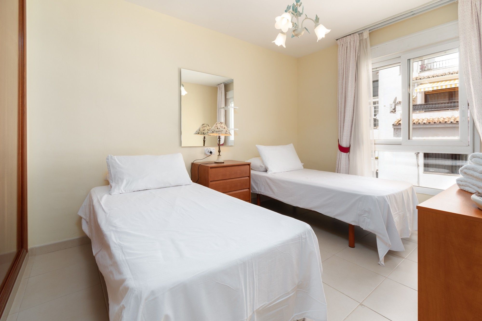 Een hotelkamer met twee bedden, een nachtkastje, een lamp, een spiegel en een raam met gordijnen.