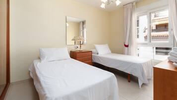 Een hotelkamer met twee bedden, een nachtkastje, een lamp, een spiegel en een raam met gordijnen.