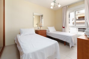 Habitación de hotel con dos camas, una mesita de noche, una lámpara, un espejo y una ventana con cortinas.