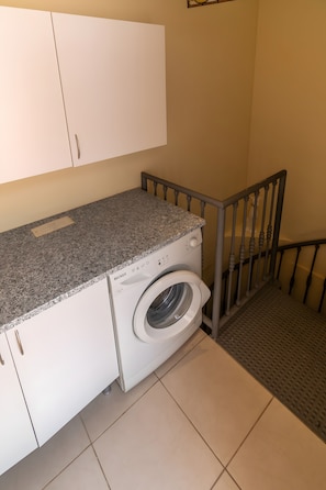 Un cuarto de lavandería con lavadora, una encimera, armarios y una escalera.