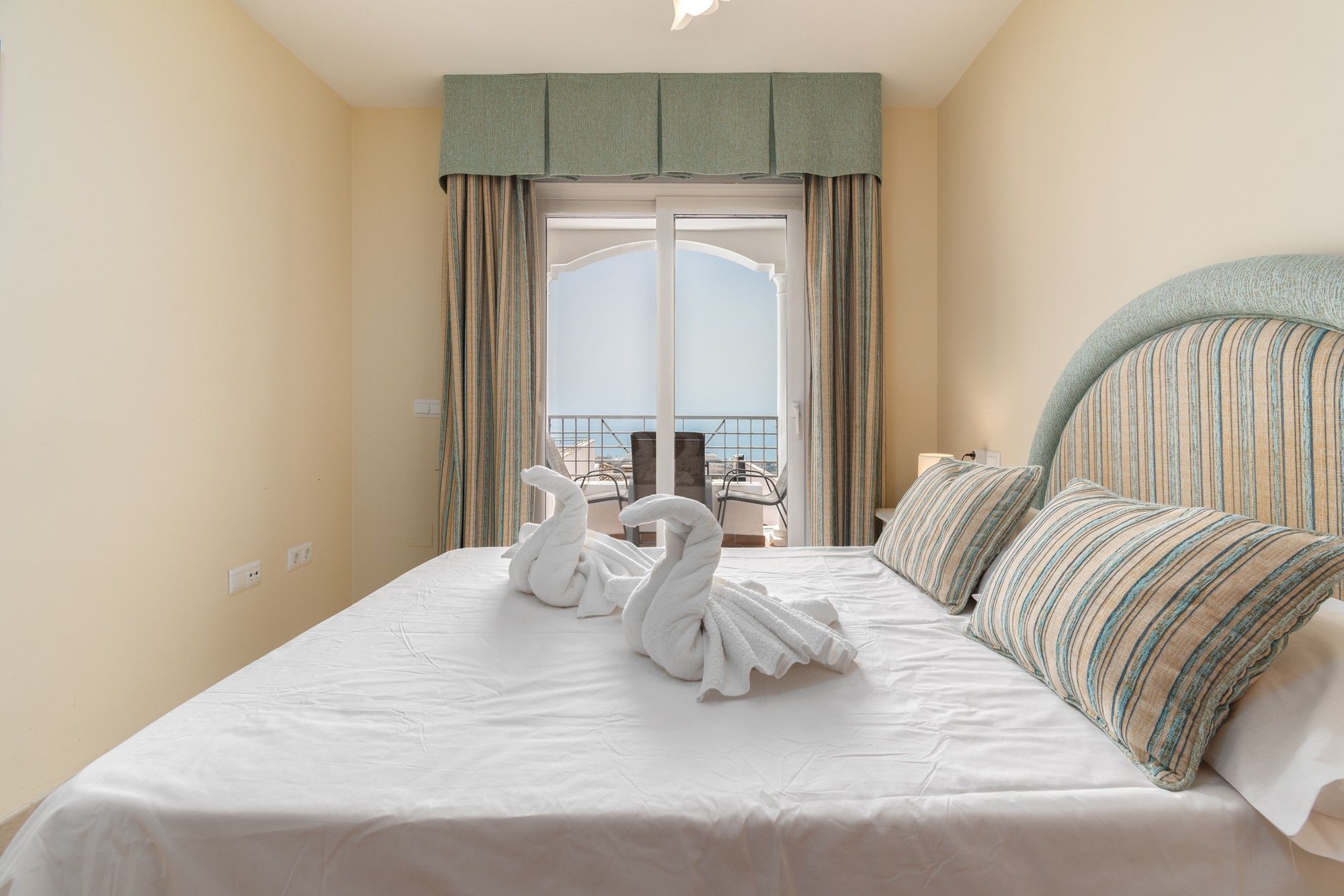 Ein Hotelzimmer mit Bett, einem Balkon mit Blick und einer Schwanen-Handtuch-Figur.