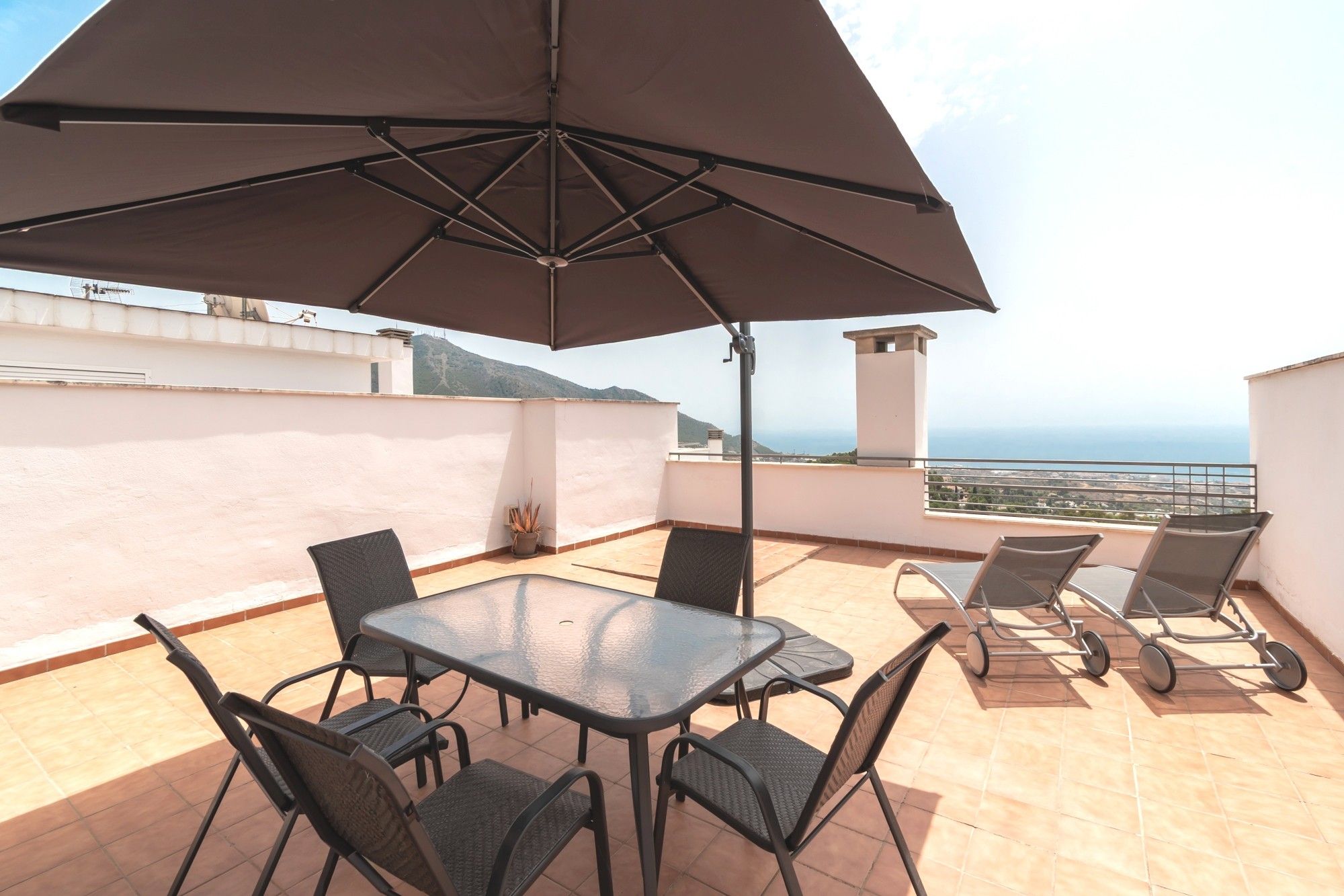 A terrace with a table and chairs, a large umbrella, and a view of the sea.