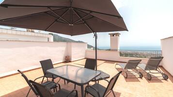 A terrace with a table and chairs, a large umbrella, and a view of the sea.