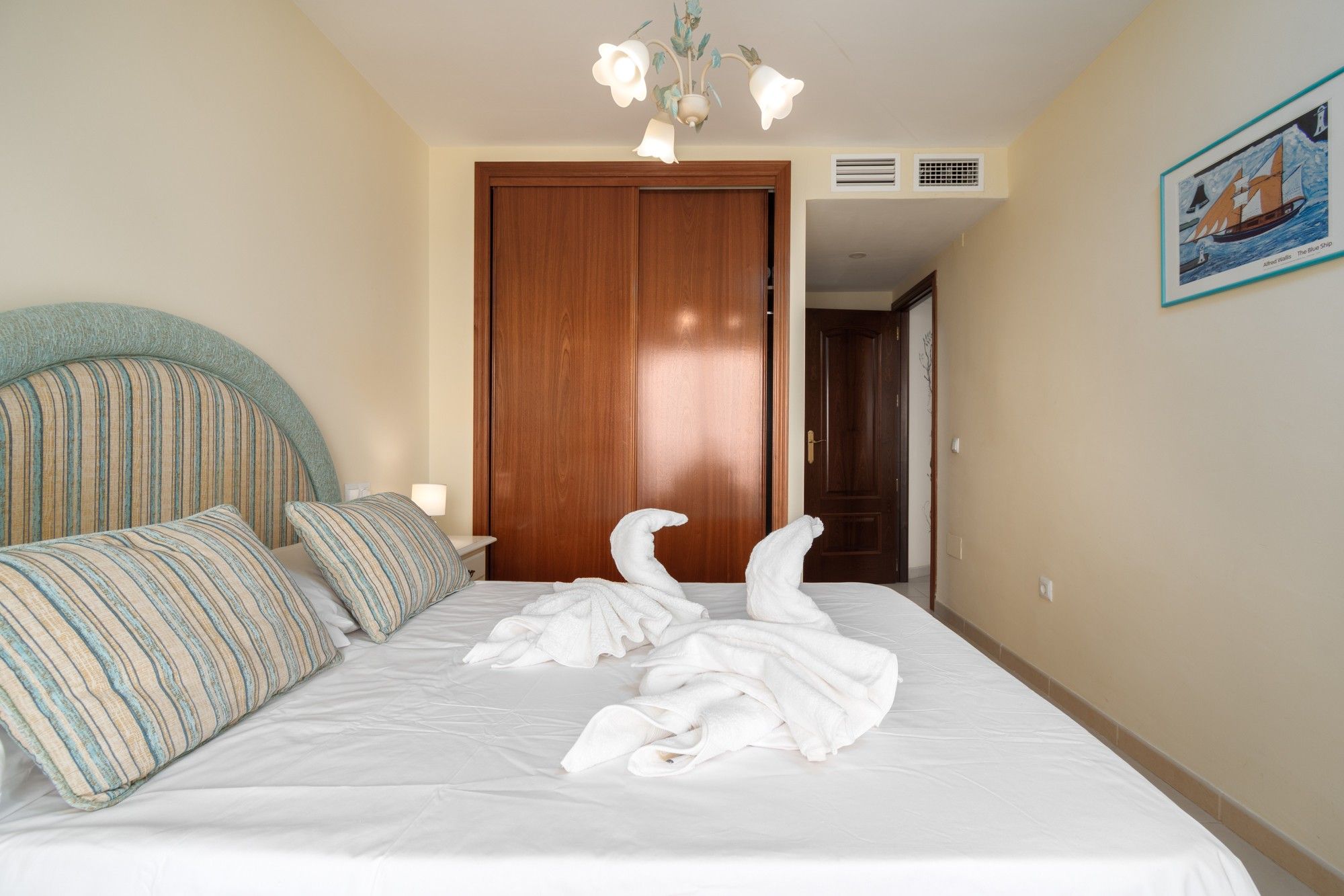 Une chambre d’hôtel avec un lit, une porte en bois, un climatiseur fixé au mur et un tableau encadré accroché au mur.