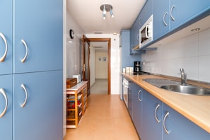 Una cocina estrecha con armarios azules, encimera de madera, pileta de acero inoxidable y un microondas.