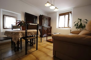 A living room with a sofa, a dining table with chairs, a TV, a cabinet, and a plant. - Country House 'El Mirador De Jozarcu' with Mountain View, Balcony and Wi-Fi (Navedo)