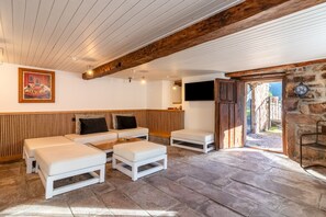 Una habitación con techo de madera, un televisor montado en una pared de piedra y un cuadro con perros en la pared.