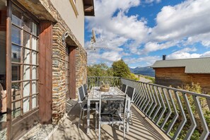 Un balcón con mesa y sillas, un muro de piedra y vistas al cielo y montañas.