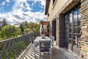A balcony with a table and chairs, overlooking a garden and a stone building. - Peaceful stay in the heart of a mountain village, with views of the pyrenees. (Égat)