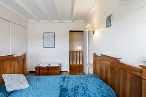 A bedroom with a wooden bed, a chest of drawers, a white door, and a wall-mounted lamp. - Peaceful stay in the heart of a mountain village, with views of the pyrenees. (Égat)