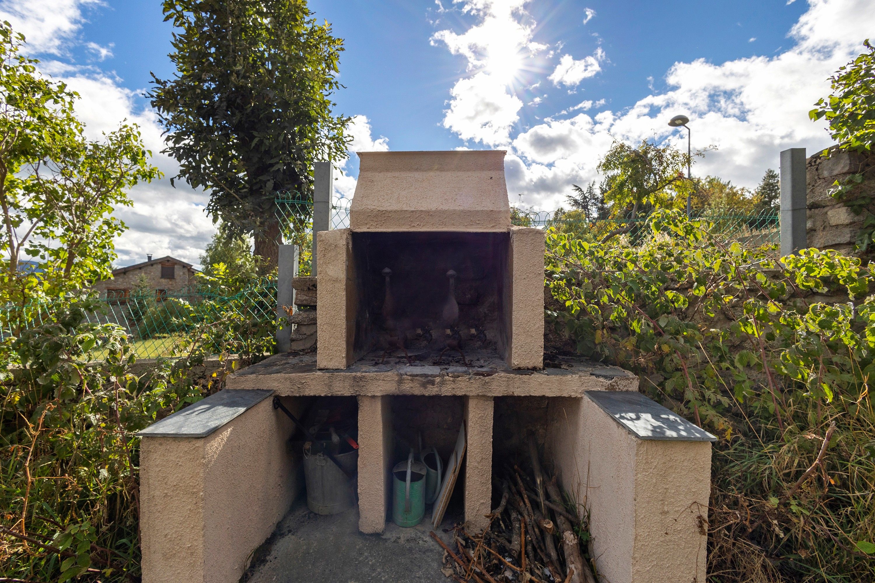 A stone structure with a chimney, surrounded by greenery and a clear sky.