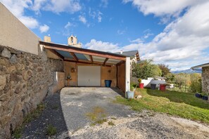 Un espacio al aire libre cubierto, con un muro de piedra, techo metálico y una puerta que da a un edificio.