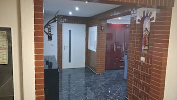 Un couloir avec une arche en briques, un sol en marbre noir, une porte blanche et une statue accrochée au mur.