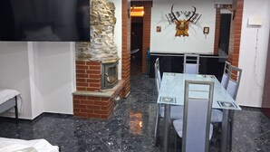 A room with a stone fireplace, a mounted deer head, a dining table with chairs, and a flat-screen TV. - Forest House with Private Terrace (Sugenheim)