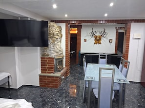 A room with a stone fireplace, a mounted deer head, a dining table with chairs, and a flat-screen TV. - Forest House with Private Terrace (Sugenheim)