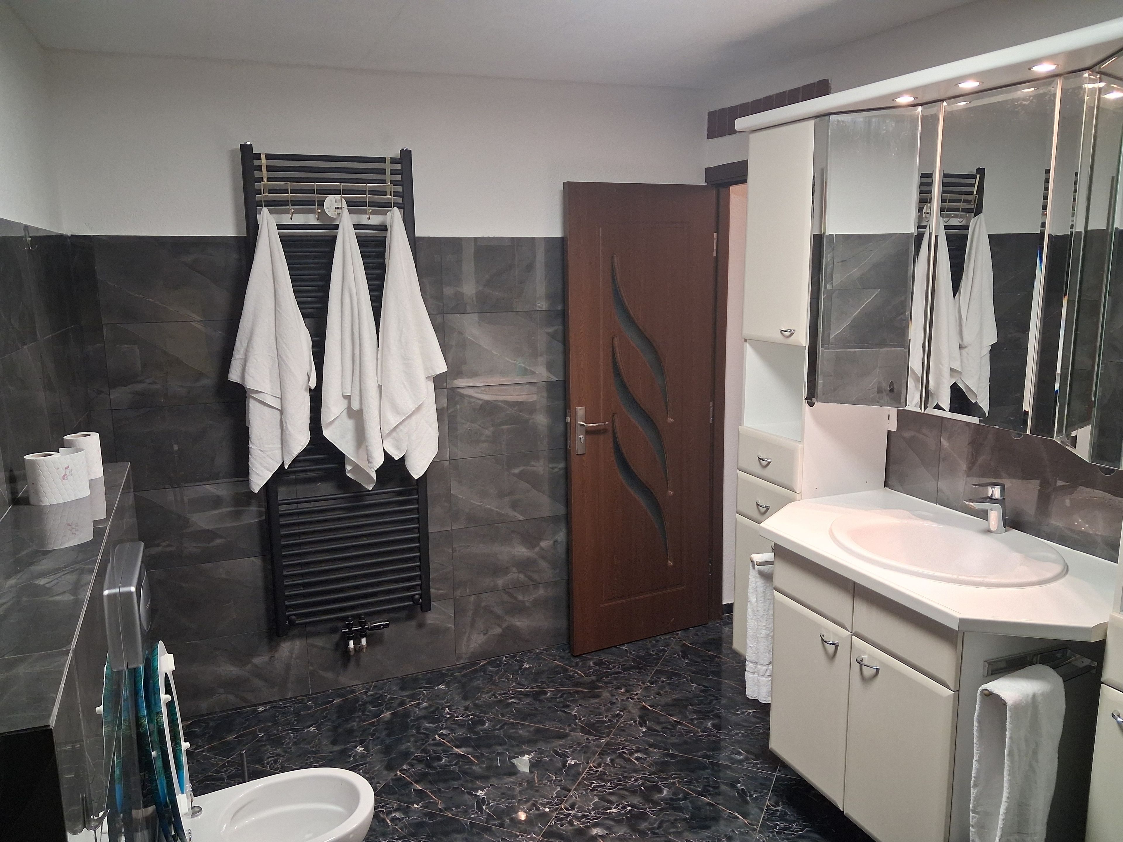 Ein modernes Badezimmer mit Marmorboden, Waschbecken in Weiß, einem großen Spiegel und einem Handtuchhalter.