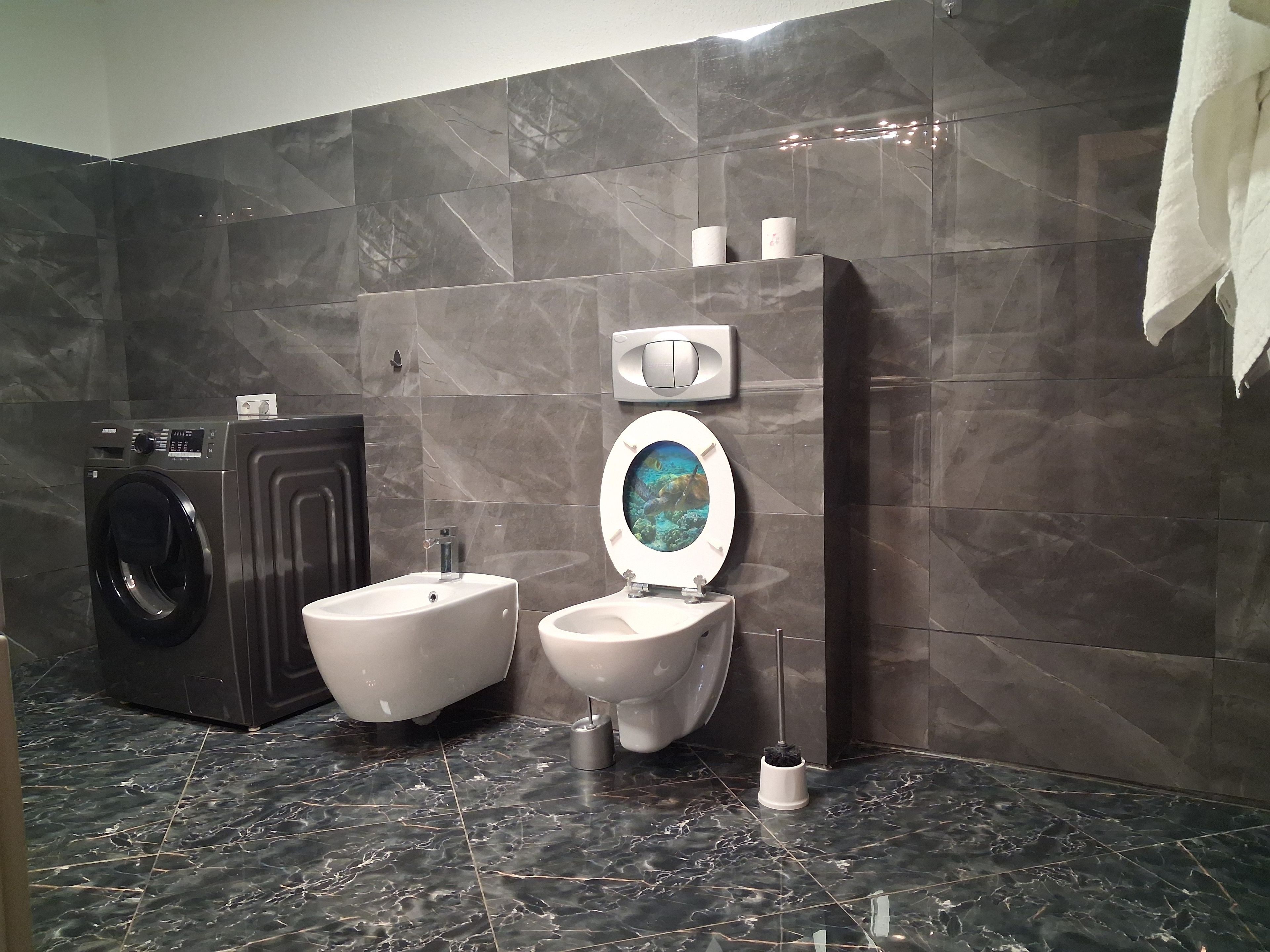 A bathroom with a washing machine, bidet, and toilet.