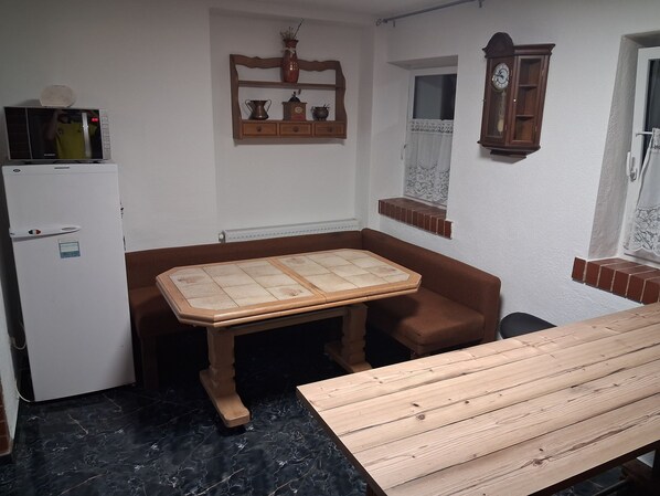 A compact kitchen with a refrigerator, a wooden table, and a cabinet with kitchenware.