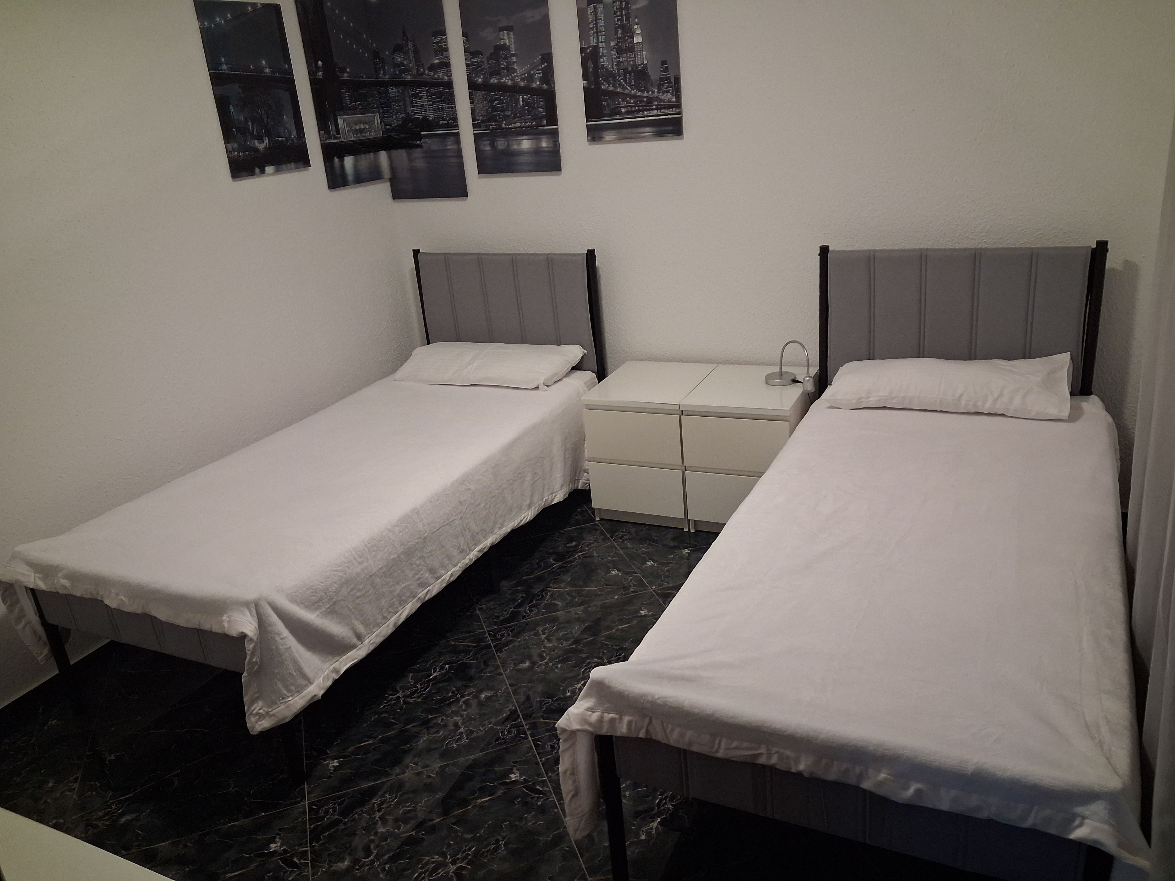 Een kamer met twee enkele bedden, een klein nachtkastje en een bedbank.