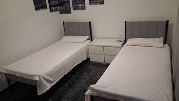 Een kamer met twee enkele bedden, een klein nachtkastje en een bedbank.