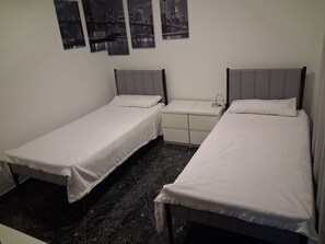 A room with two single beds, a small bedside table, and a nightstand.