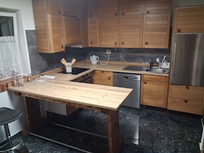 A kitchen with wooden cabinets, a stainless steel refrigerator, a dishwasher, and a marble countertop.