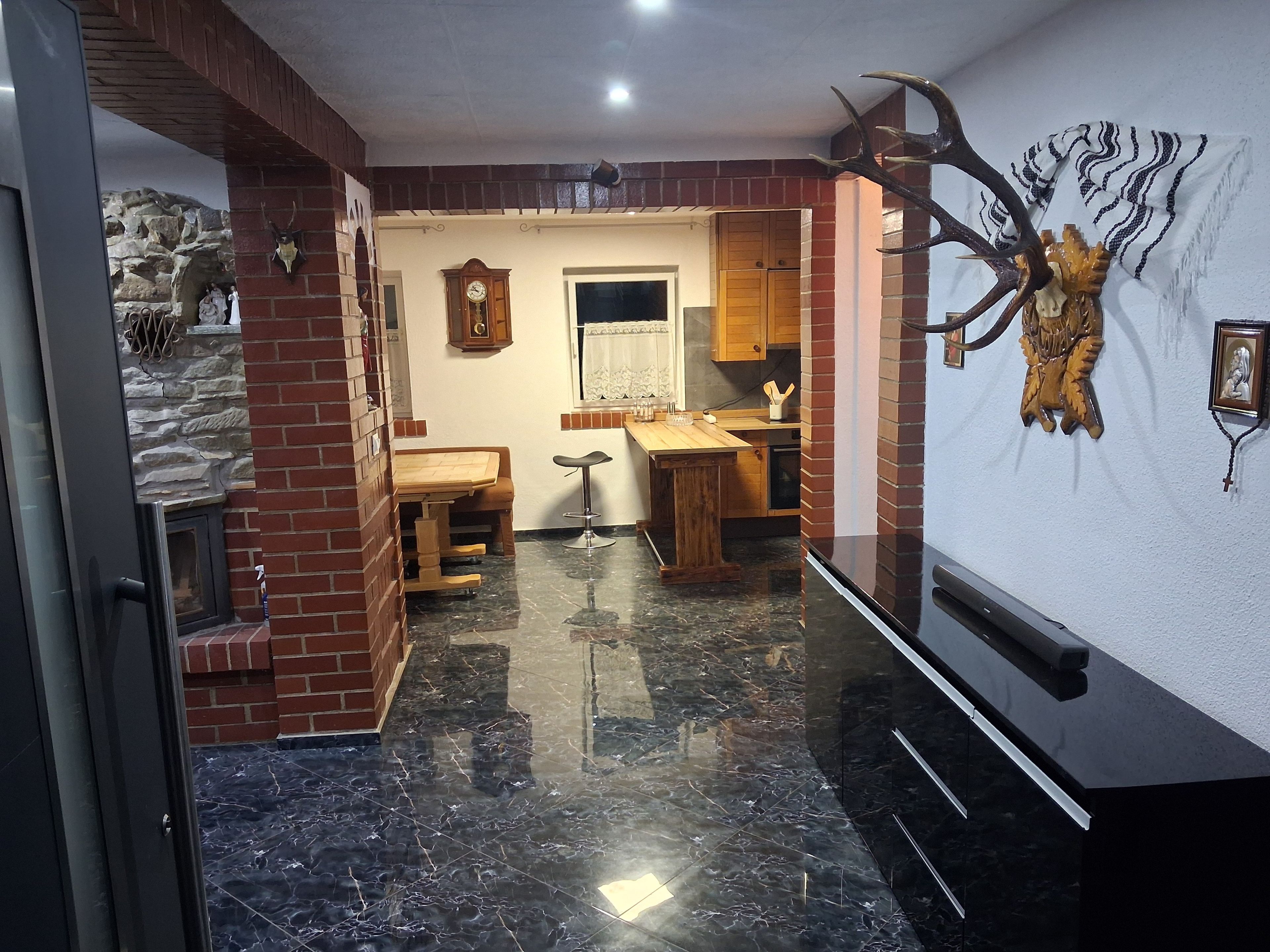 A kitchen with a stone wall, wooden cabinets, a marble floor, and a clock.