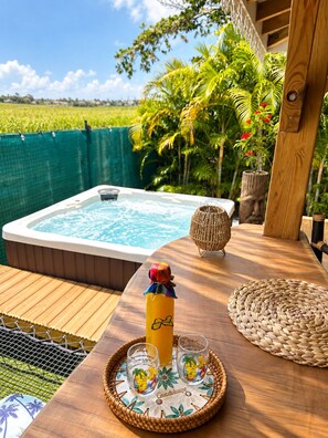A wooden deck with a hot tub, a woven mat, and a tray with glasses and a bottle.