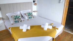 A bed with white bedding, two decorative pillows, a yellow throw blanket, and rolled towels.