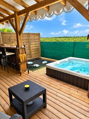 A wooden deck with a hot tub, outdoor seating, and a view of a green field.