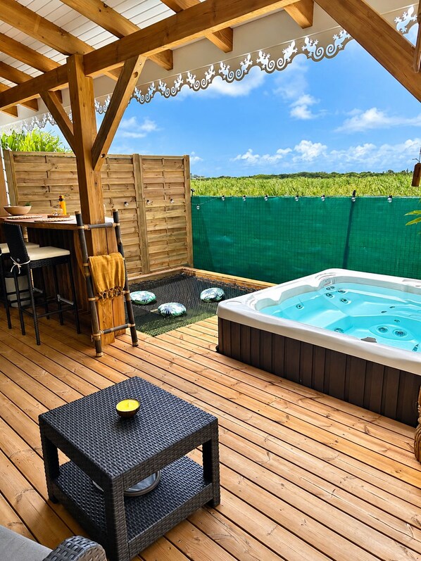 A wooden deck with a hot tub, outdoor seating, and a view of a green field.