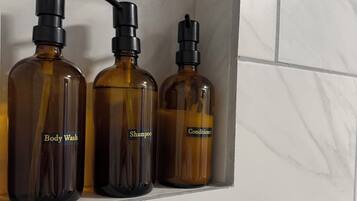 Three bottles of body wash, shampoo, and conditioner on a shelf against a tiled wall.