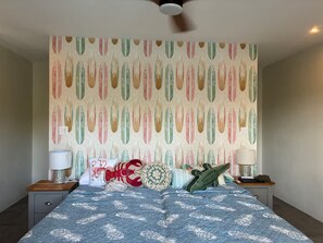 Un dormitorio con cama, mesitas de noche, ventilador de techo y una pared con estampado de papel.