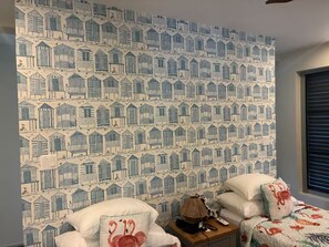 Ein Schlafzimmer mit einem gemusterten Wandpapier, einem Bett mit floralem Bettzeug und einem Nachttisch mit Lampe und Fernbedienung.