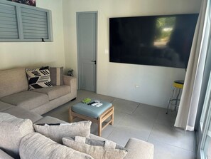 Una sala de estar con un sofá, una mesa de centro, un televisor montado en la pared y una puerta.