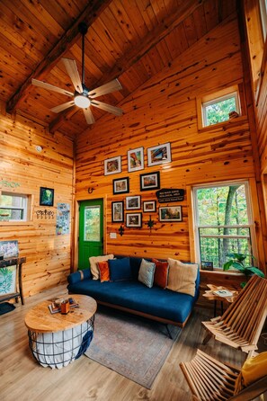 L’intérieur chaleureux d’un chalet avec un plafond en bois, un ventilateur de plafond, un canapé bleu, une table basse et des tableaux encadrés accrochés aux murs.