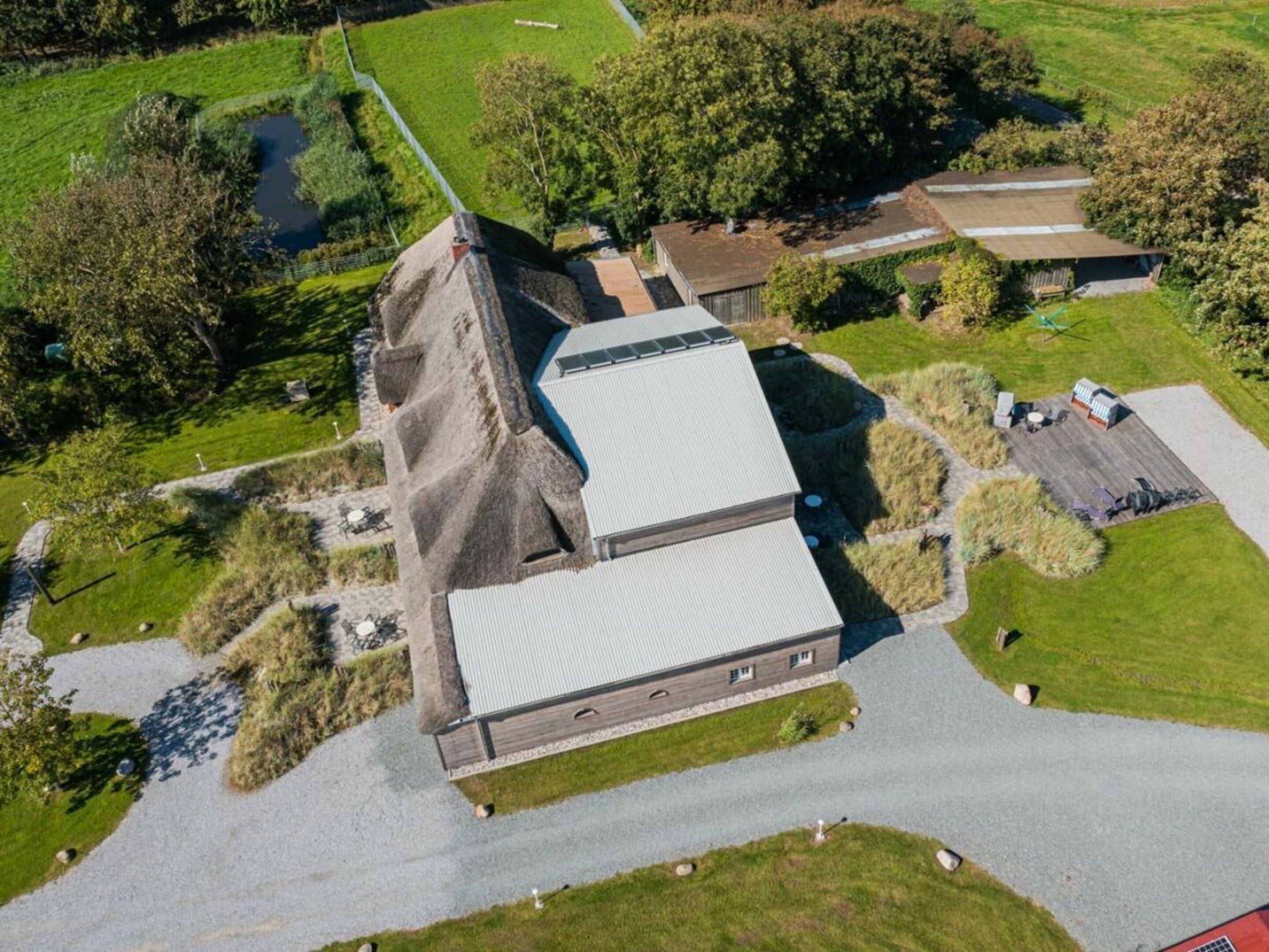 Vue aérienne d’un bâtiment doté d’un toit en pente, entouré d’une pelouse bien entretenue et d’un petit étang.