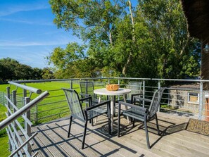 Eine Terrasse mit Tisch und Stühlen, mit Blick auf eine Wiese und Bäume.