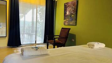 Une chambre d’hôtel avec un lit, une chaise, une fenêtre avec des rideaux et un tableau au mur.