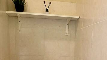 A small bathroom with a toilet, a trash bin, and a shelf with a plant and a bottle.